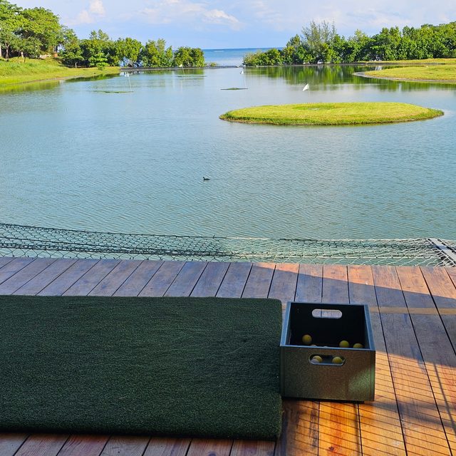 A hitting mat and a crate of range balls facing target greens floating in a lagoon