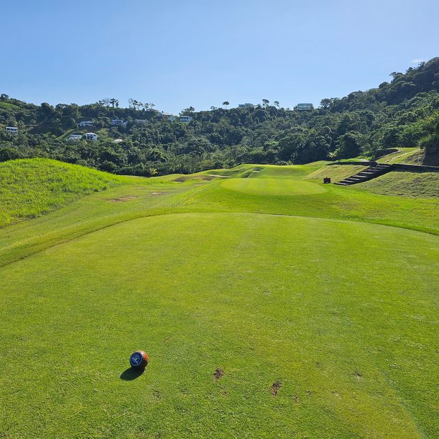 A tee box with a marker, the fairway climbing toward jungle-covered hills