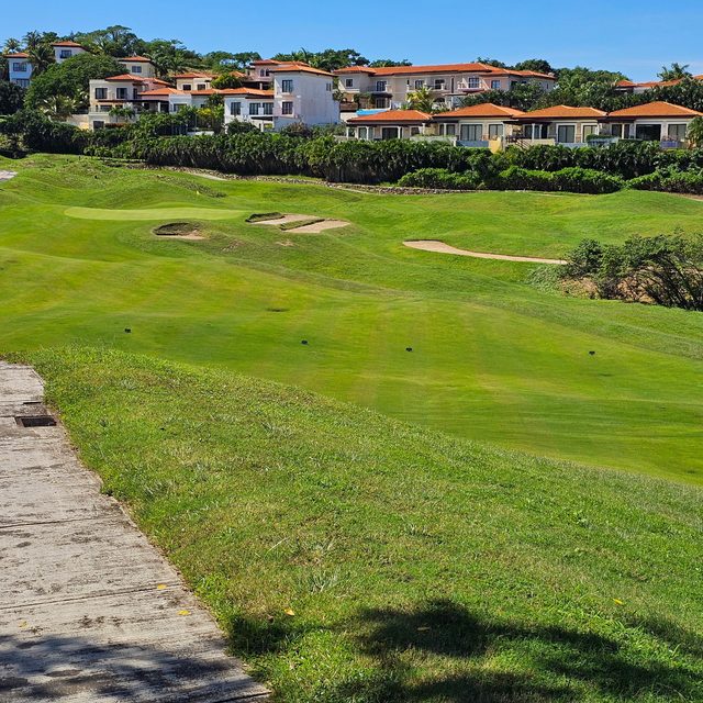 A fairway rolling up toward a green and bunkers, with terracotta-roofed villas on the hill above