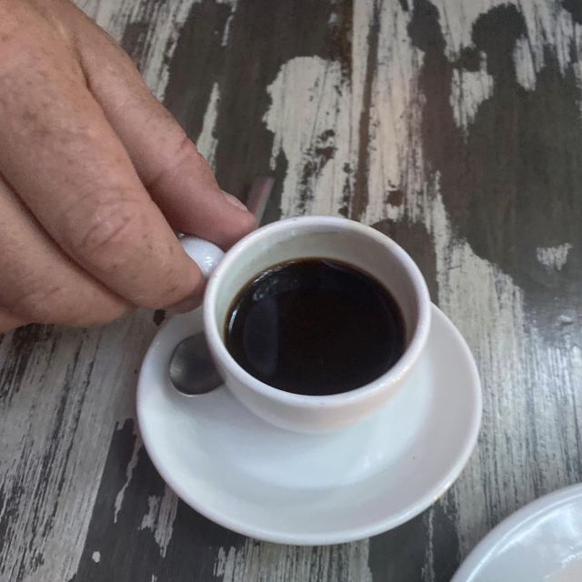 Gunny holding a small cup of black coffee on a weathered table