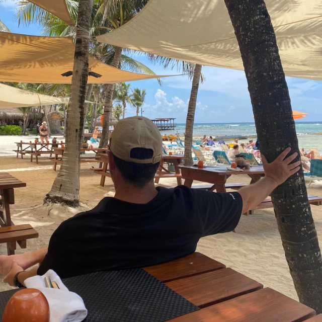 Gunny relaxing at a shaded beach table, looking out at the water