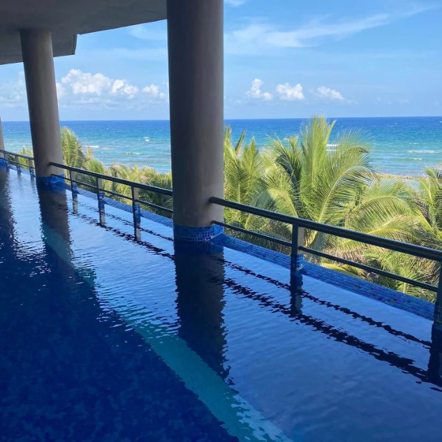 A swim-up pool running along the length of a resort floor, with the ocean beyond