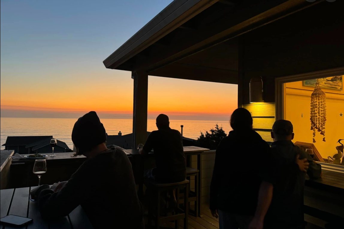 The crew in silhouette on a covered deck, watching the sun set over the Pacific
