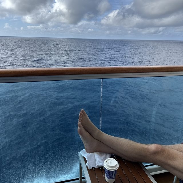 Bare feet up on the balcony table, coffee cup beside them, open ocean past the glass railing