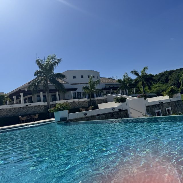 The white clubhouse above the infinity pool, green hills behind
