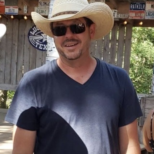 Gunny in a straw cowboy hat and sunglasses, smiling outside a Texas bar