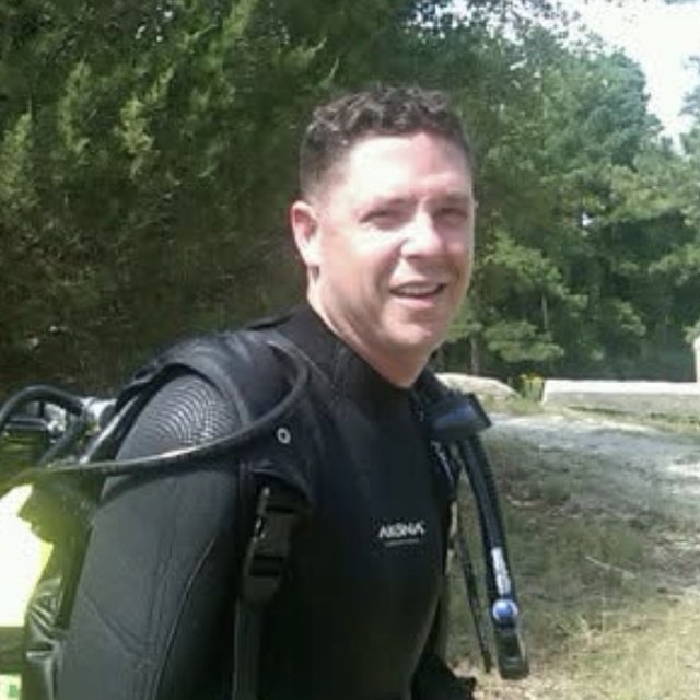 Gunny in a wetsuit with a tank on his back, grinning before a dive