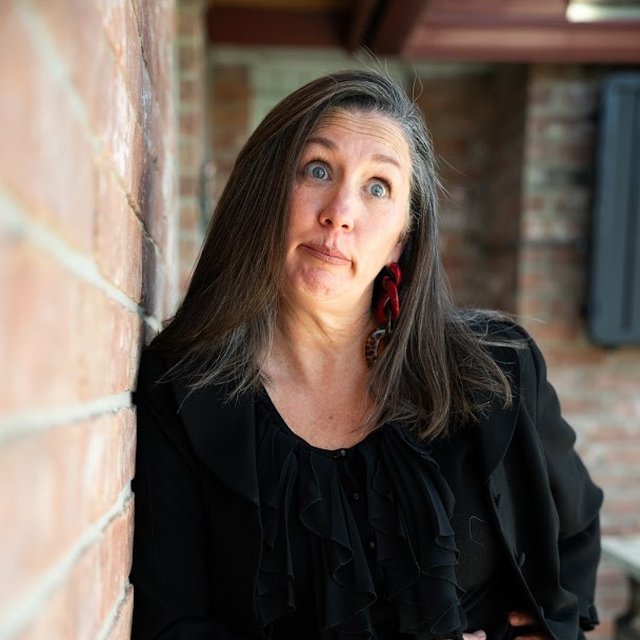 Nikki in black against a brick wall, making a face at the camera