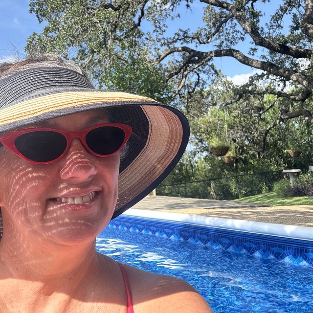 Nikki in a sun hat and red cat-eye sunglasses beside a pool