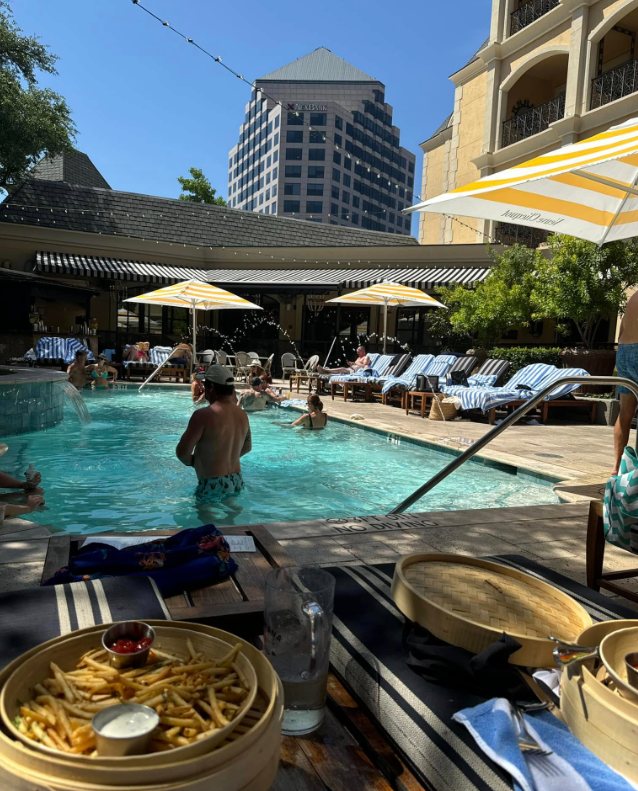 Fries served in a bamboo steamer beside the hotel pool, with cabanas and striped umbrellas