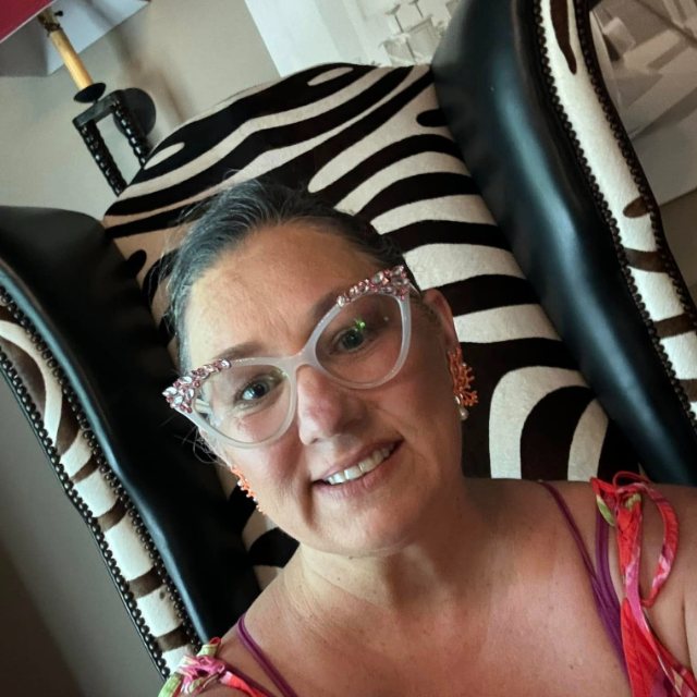 Nikki smiling in jeweled cat-eye glasses, settled into a zebra-print wingback chair